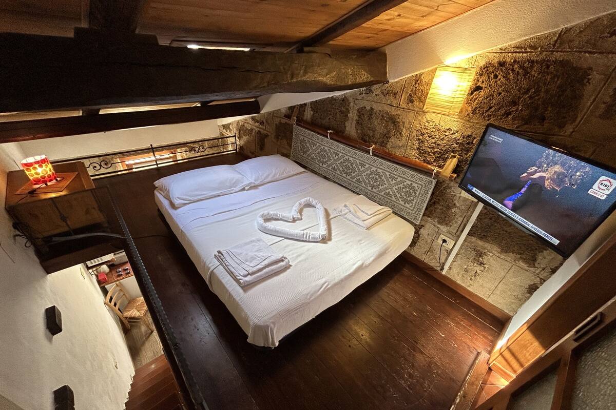 A cozy room with a bed, a TV, and a stone wall.