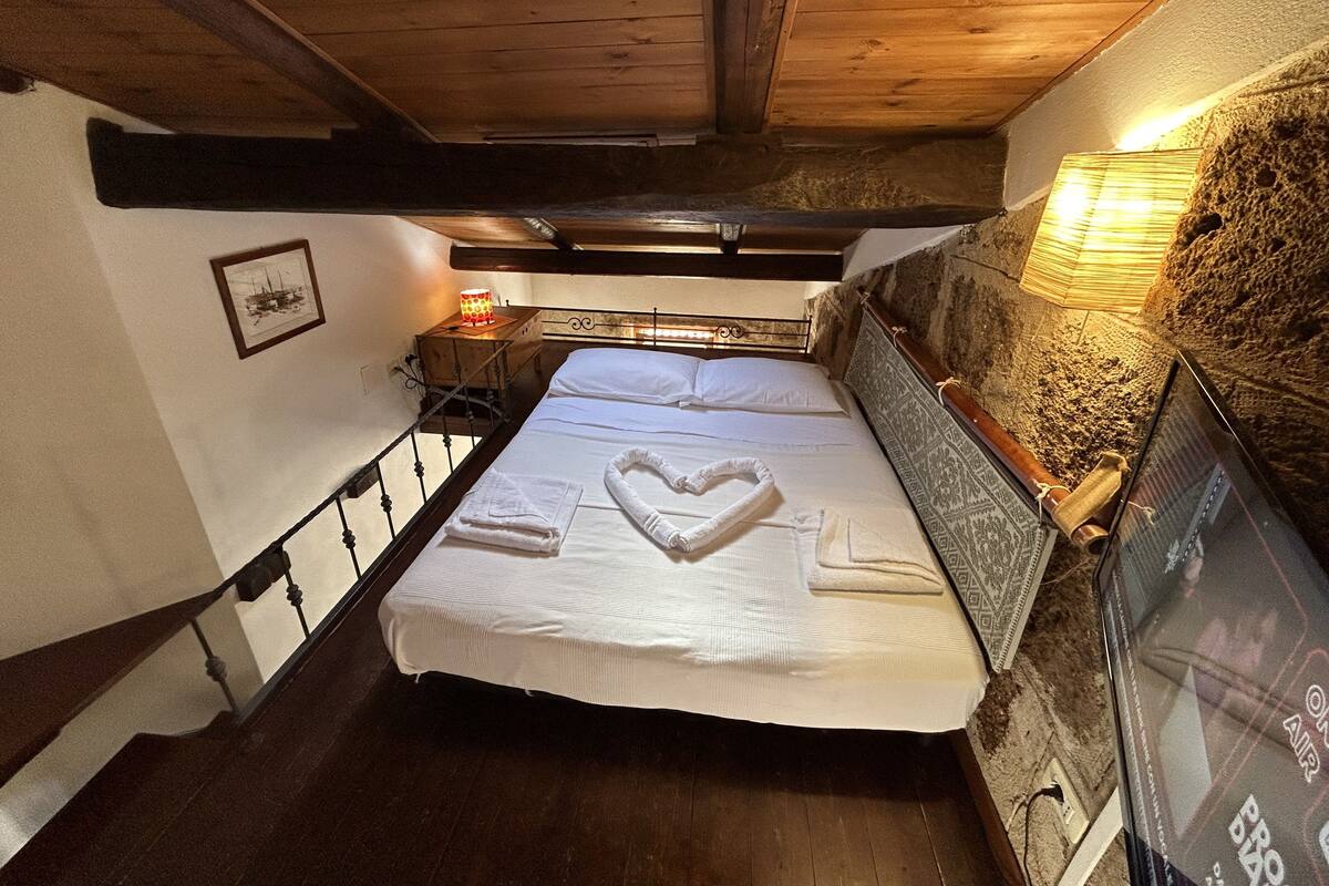 A bedroom with a wooden ceiling, a bed with white linens, a bedside lamp, and a framed picture on the wall.