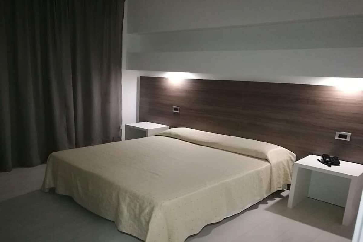 A modern hotel room with a large bed, two bedside tables, and a headboard with integrated lighting.