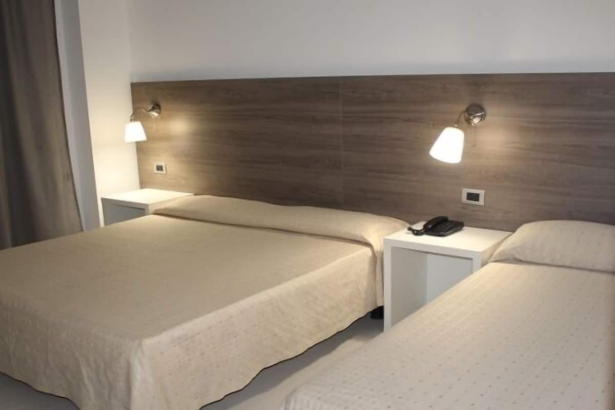 A hotel room with two single beds, a nightstand with a phone, and wall-mounted lamps.