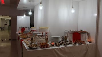 A buffet table with various food items and a cake, set against a white backdrop with hanging light bulbs.