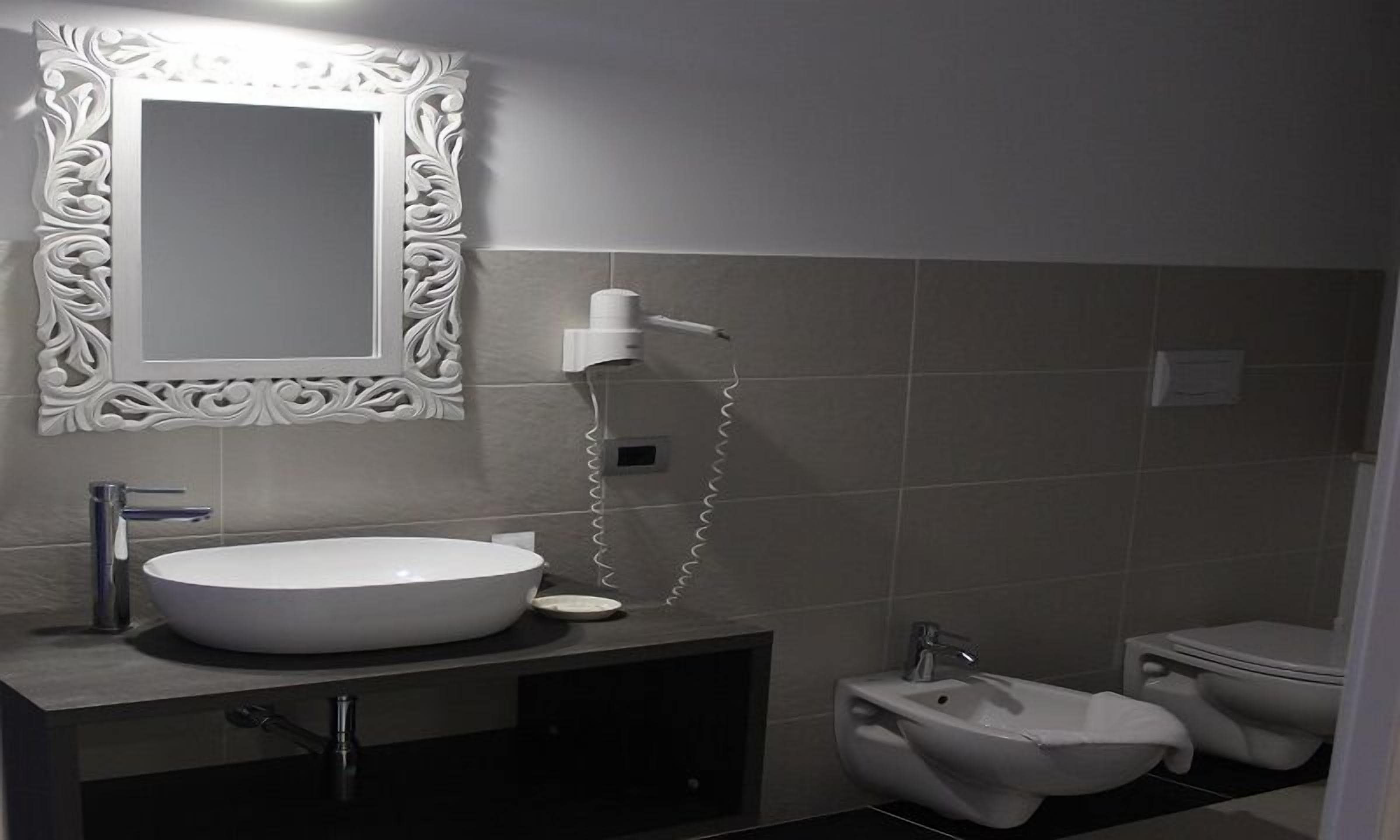 A modern bathroom with a large white sink, a mirror with ornate frame, and a bidet.