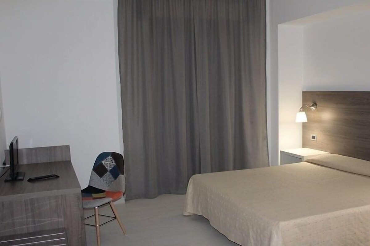 A hotel room with a bed, a desk, a chair, and a curtain.