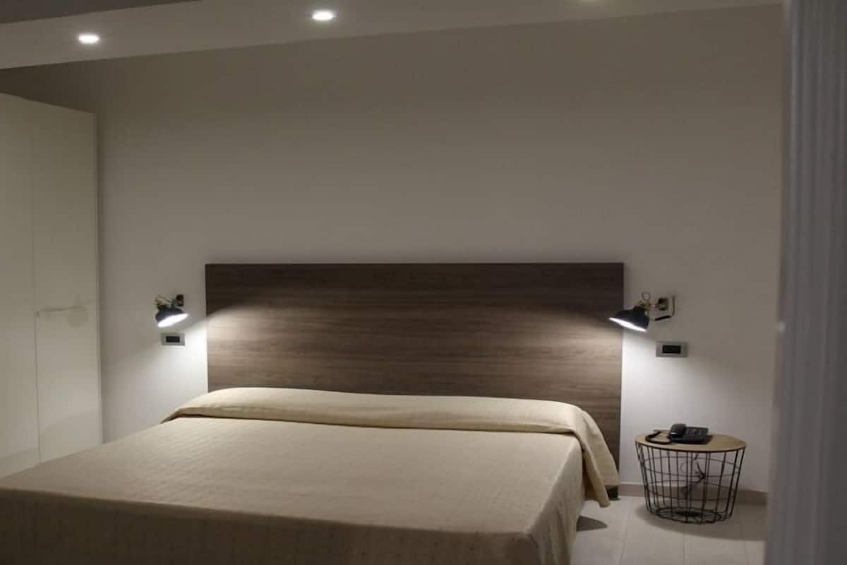 A modern bedroom with a large bed, two bedside lamps, a small round table with a phone, and a white wardrobe.