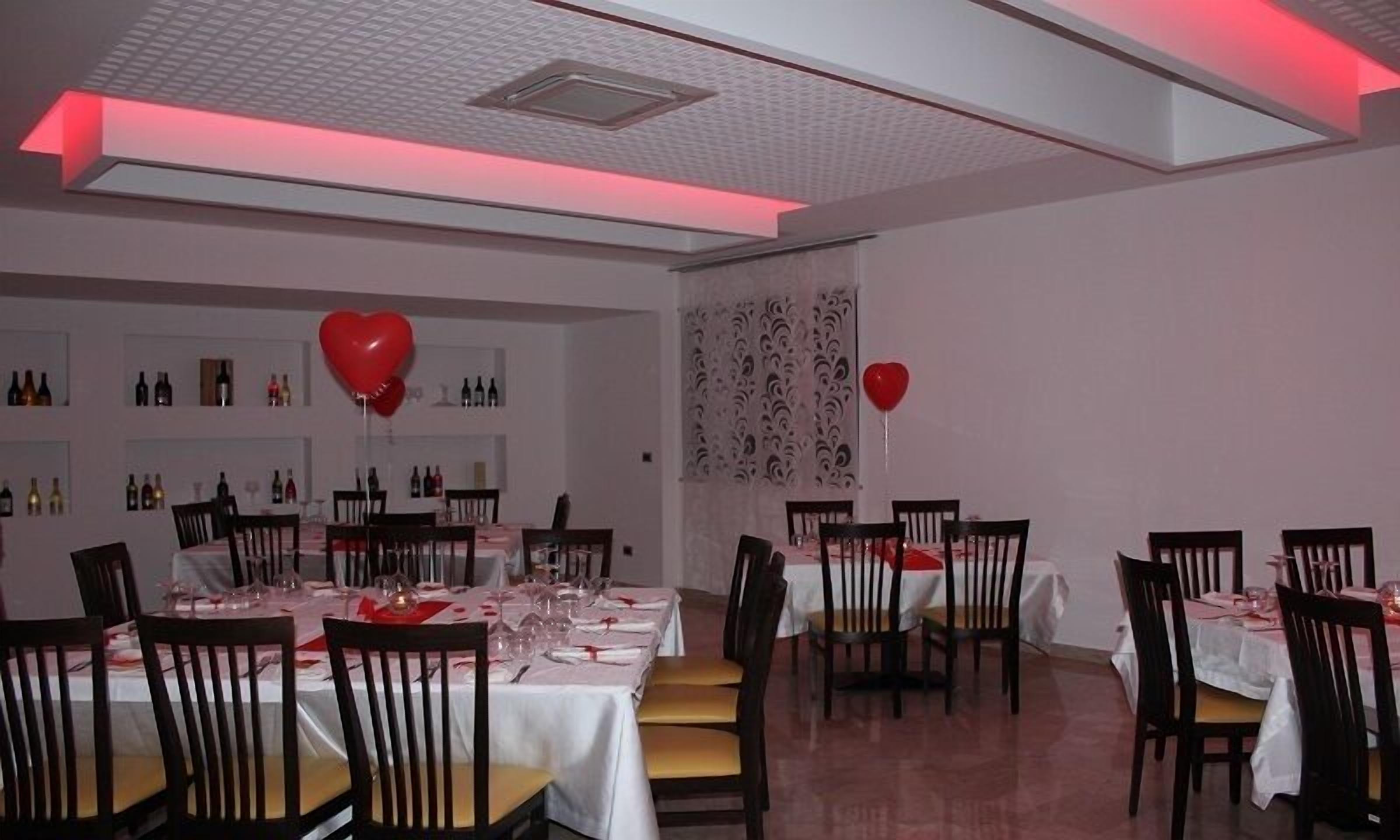 A dining area with tables set for two, featuring white tablecloths and red heart-shaped balloons.
