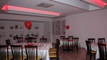 A dining area with tables set for two, featuring white tablecloths and red heart-shaped balloons.