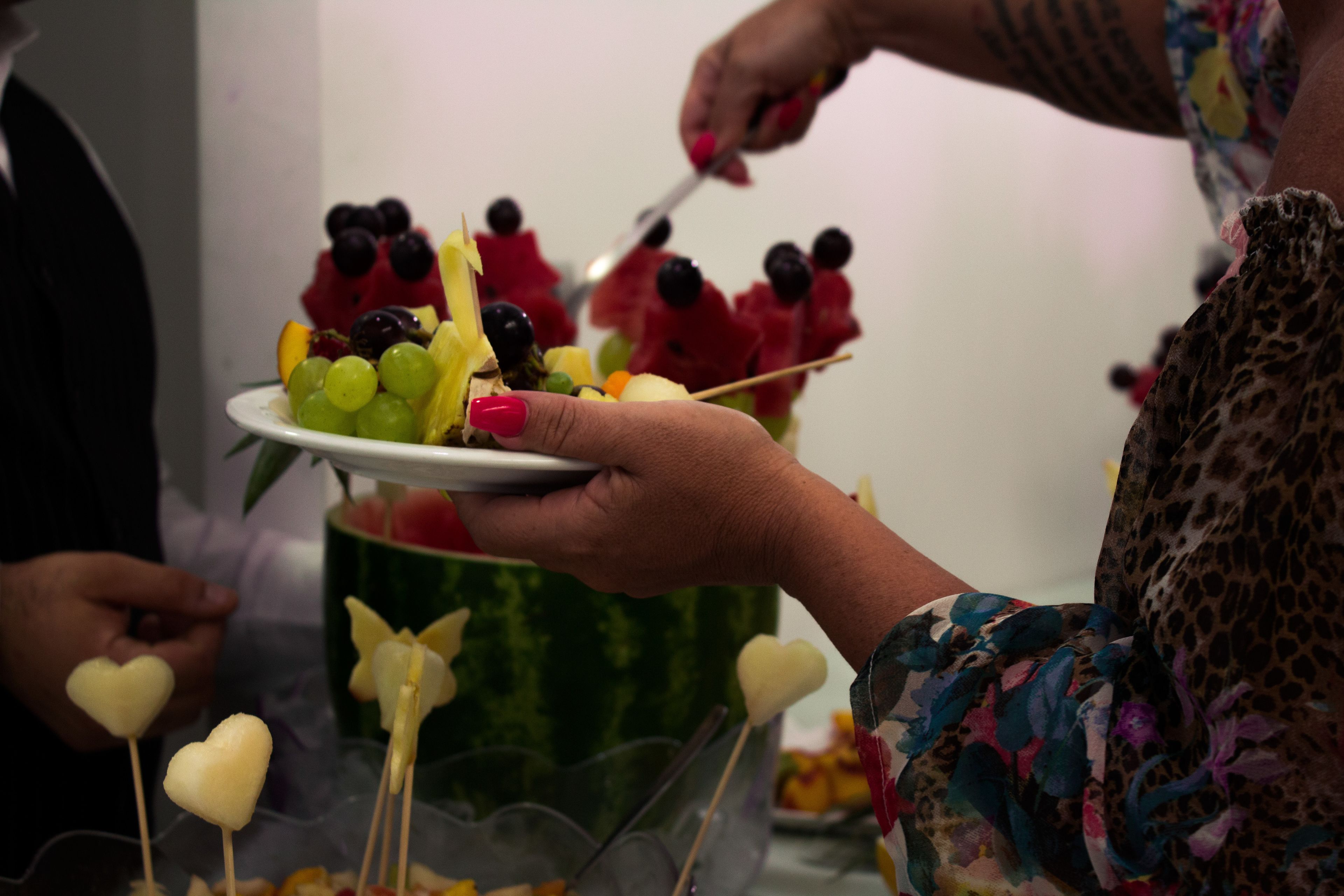 A person holding a plate with fruit skewers and a watermelon.