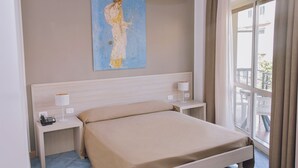 Quarto com cama, mesas de cabeceira, luminária, pintura e janela com cortinas.