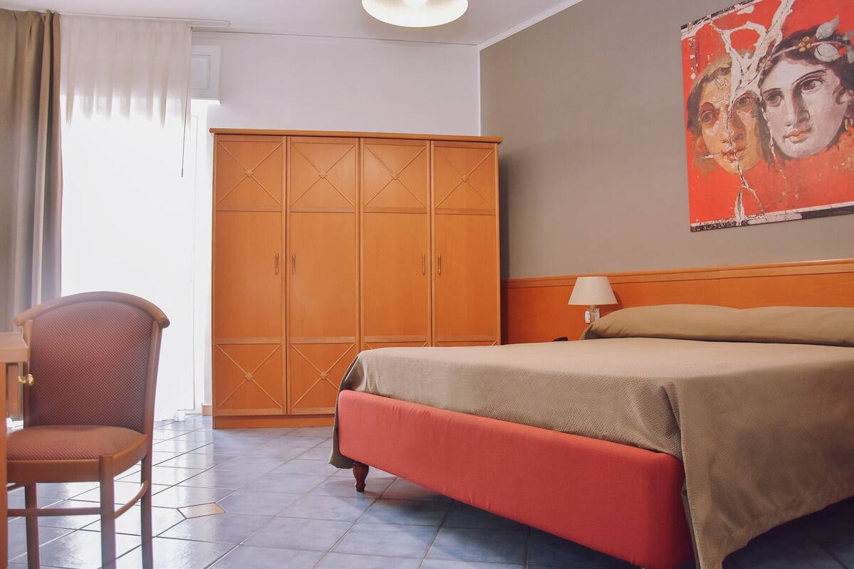 A bedroom with a bed, a chair, a wardrobe, and a painting on the wall.