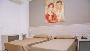 Quarto de hotel com duas camas de solteiro, uma mesa de cabeceira com abajur, uma pequena mesa com telefone e um quadro na parede.