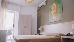 Quarto de hotel com uma cama, uma escrivaninha com telefone, uma luminária e um quadro na parede.