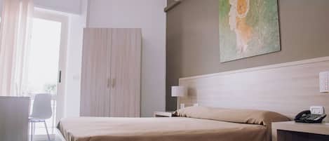 Una habitación de hotel con una cama, un escritorio con teléfono, una lámpara y un cuadro en la pared.