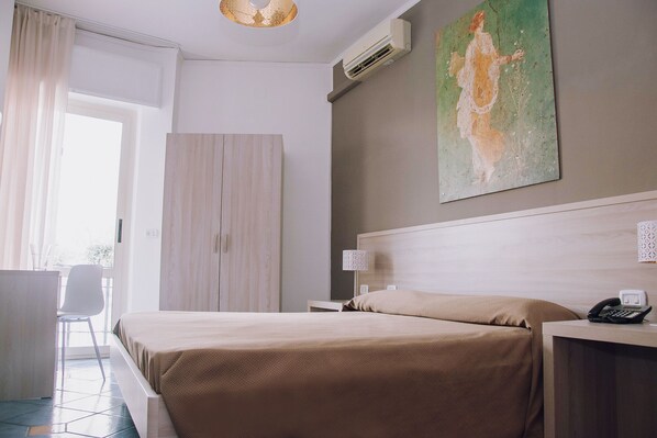 Una habitación de hotel con una cama, un escritorio con teléfono, una lámpara y un cuadro en la pared.