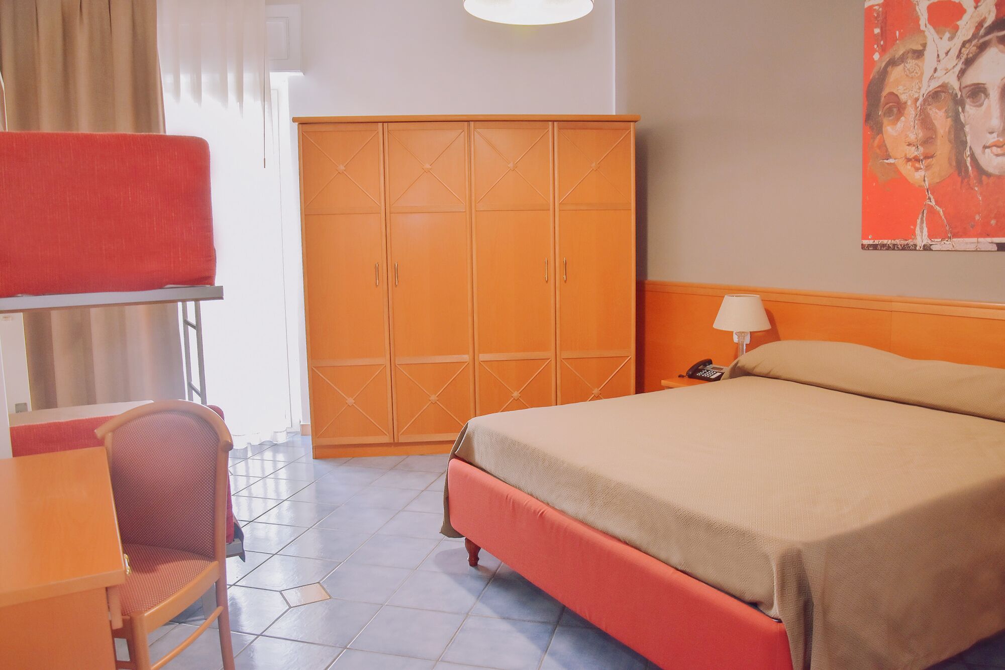 Une chambre d’hôtel comprenant un lit, un bureau avec une chaise, une armoire et une lampe.