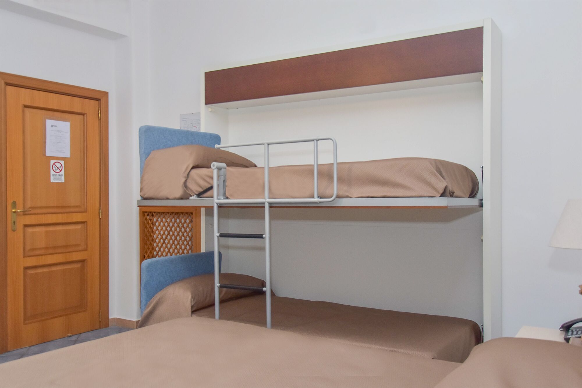 Una stanza con un letto a castello, una porta in legno, un tavolino e una lampada.