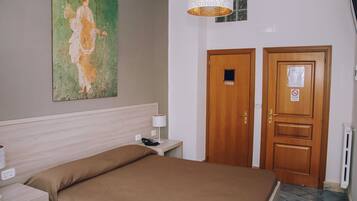 Ein Hotelzimmer mit einem Bett, einem Nachttisch, einer Lampe, einem Bild an der Wand und einer Tür mit einem Schild.