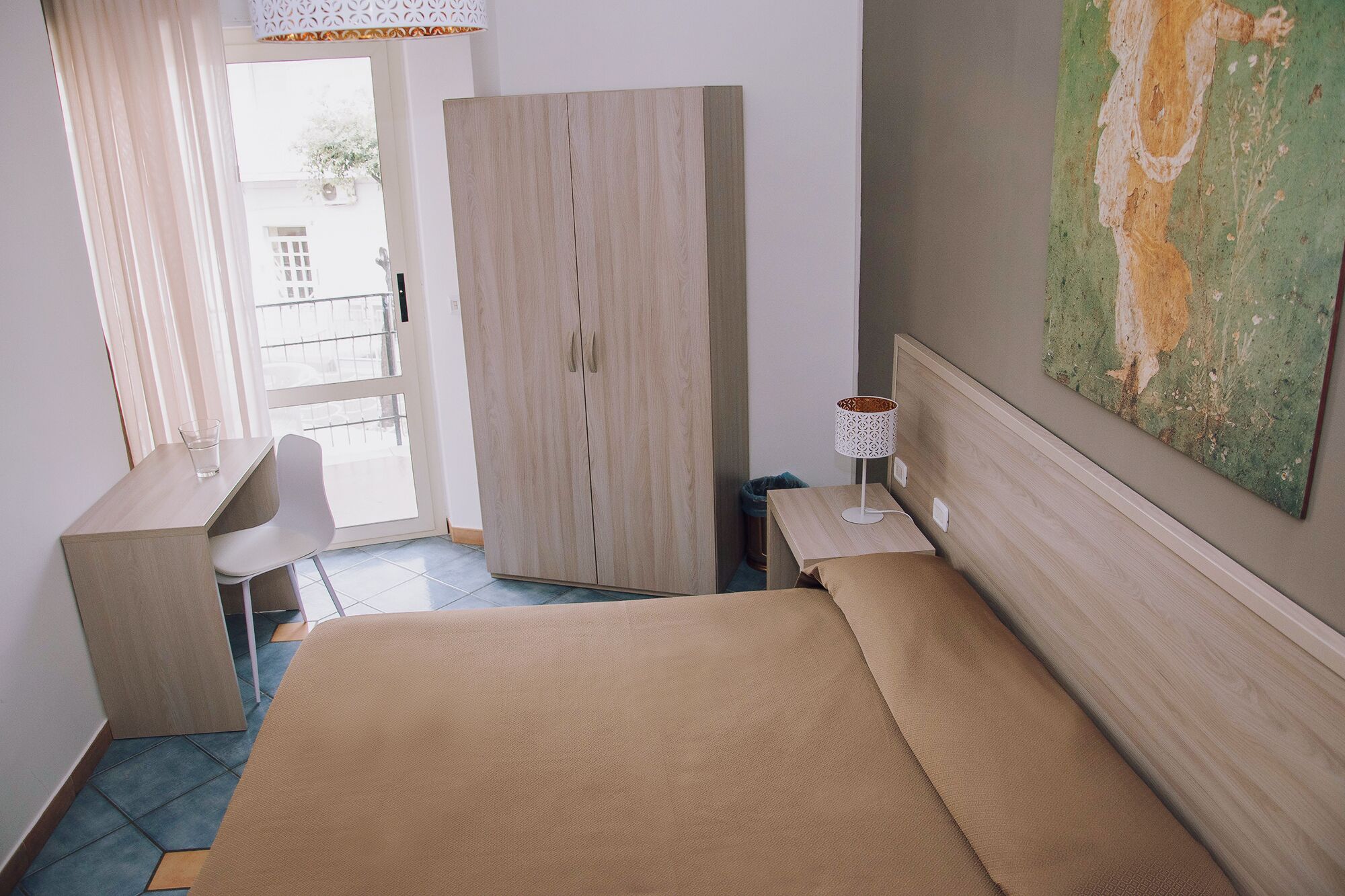 Ein Hotelzimmer mit Bett, Schreibtisch, Stuhl, Lampe und einem Bild an der Wand.