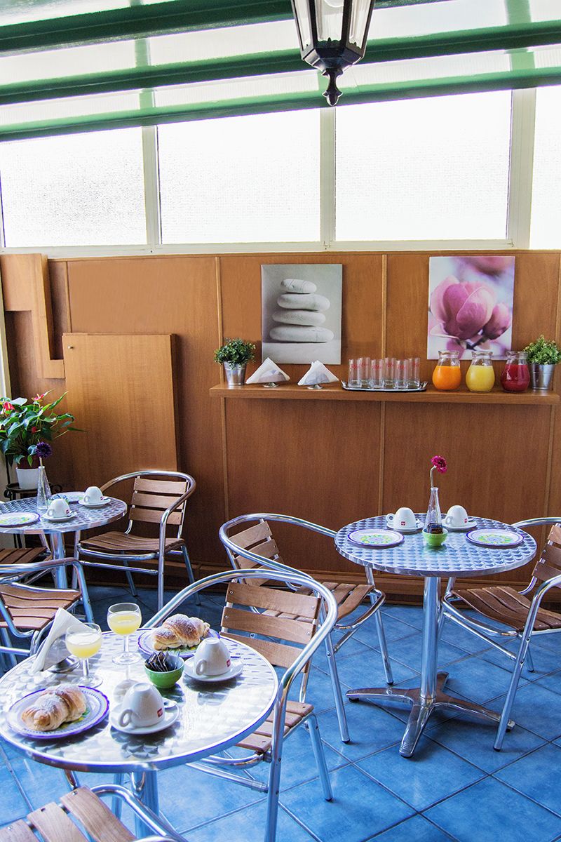 Ein Café mit runden Tischen und Stühlen, Frühstücksangebot und einer Wand mit einem Blumenbild sowie einem Stapel Handtüchern.