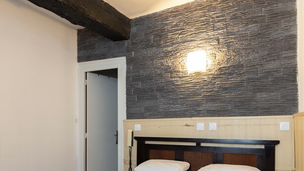 A hotel room with a bed, a wooden headboard, a stone wall, and a light fixture. - Hôtel du Bellay (Blois)