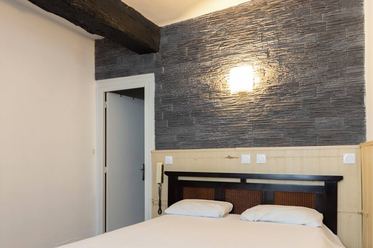 A hotel room with a bed, a wooden headboard, a stone wall, and a light fixture.