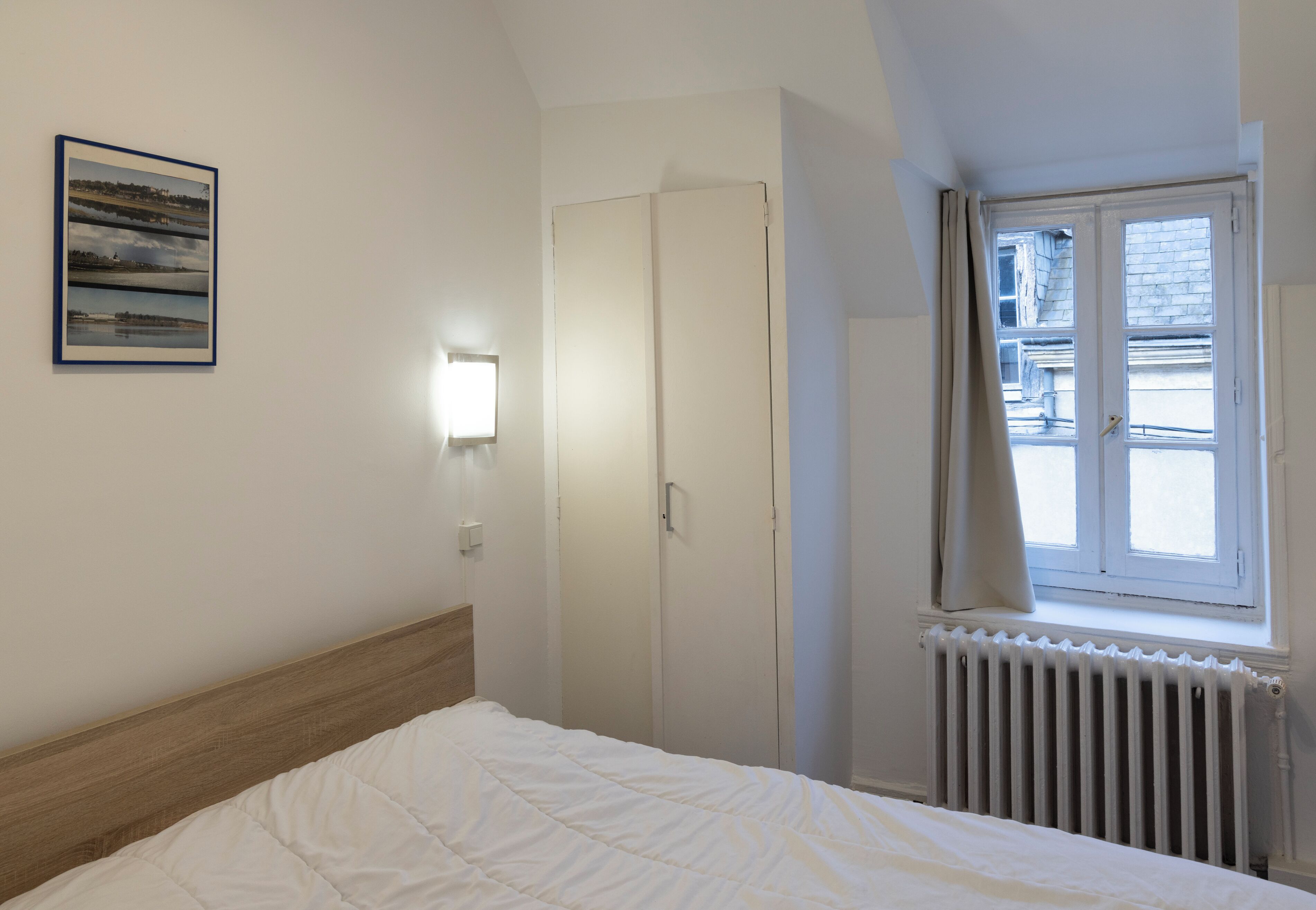 A bedroom with a bed, a wardrobe, a radiator, and a window with curtains.