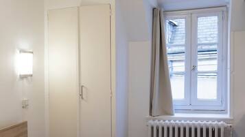 Een slaapkamer met een bed, een radiator, een raam met gordijnen, een deur en een wandlamp.
