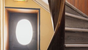 A wooden staircase with a circular window and a green emergency exit sign. - Hôtel du Bellay (Blois)