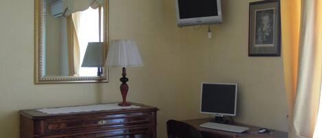 Una habitación con un tocador de madera, un escritorio con computadora, un espejo y un cuadro en la pared.