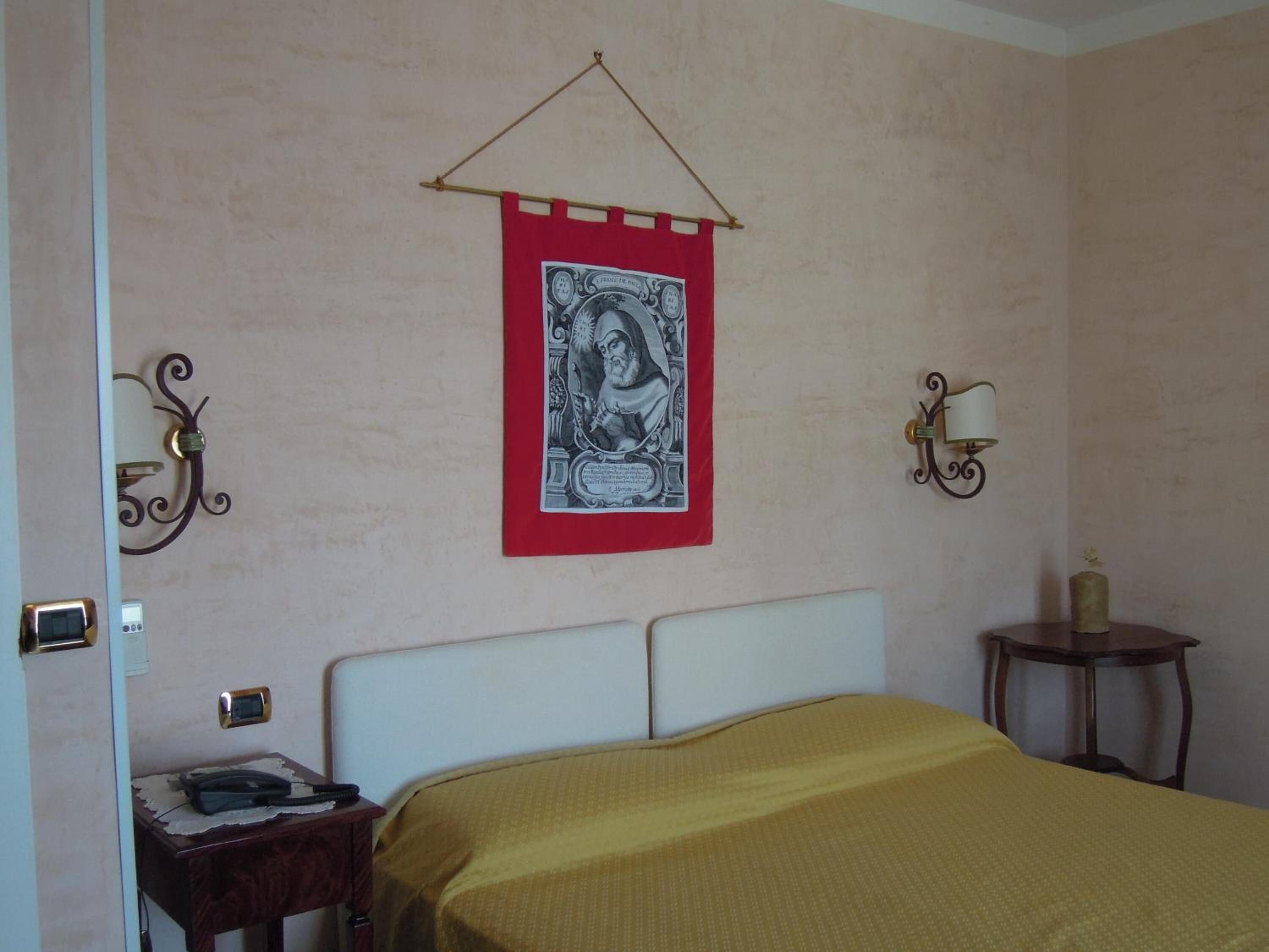 A bedroom with a bed, a bedside table, a lamp, and a wall hanging.