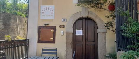 A building with a sign for 'Sant'Agostino Guest Rooms', a wooden door, a small window, and a table with chairs outside.