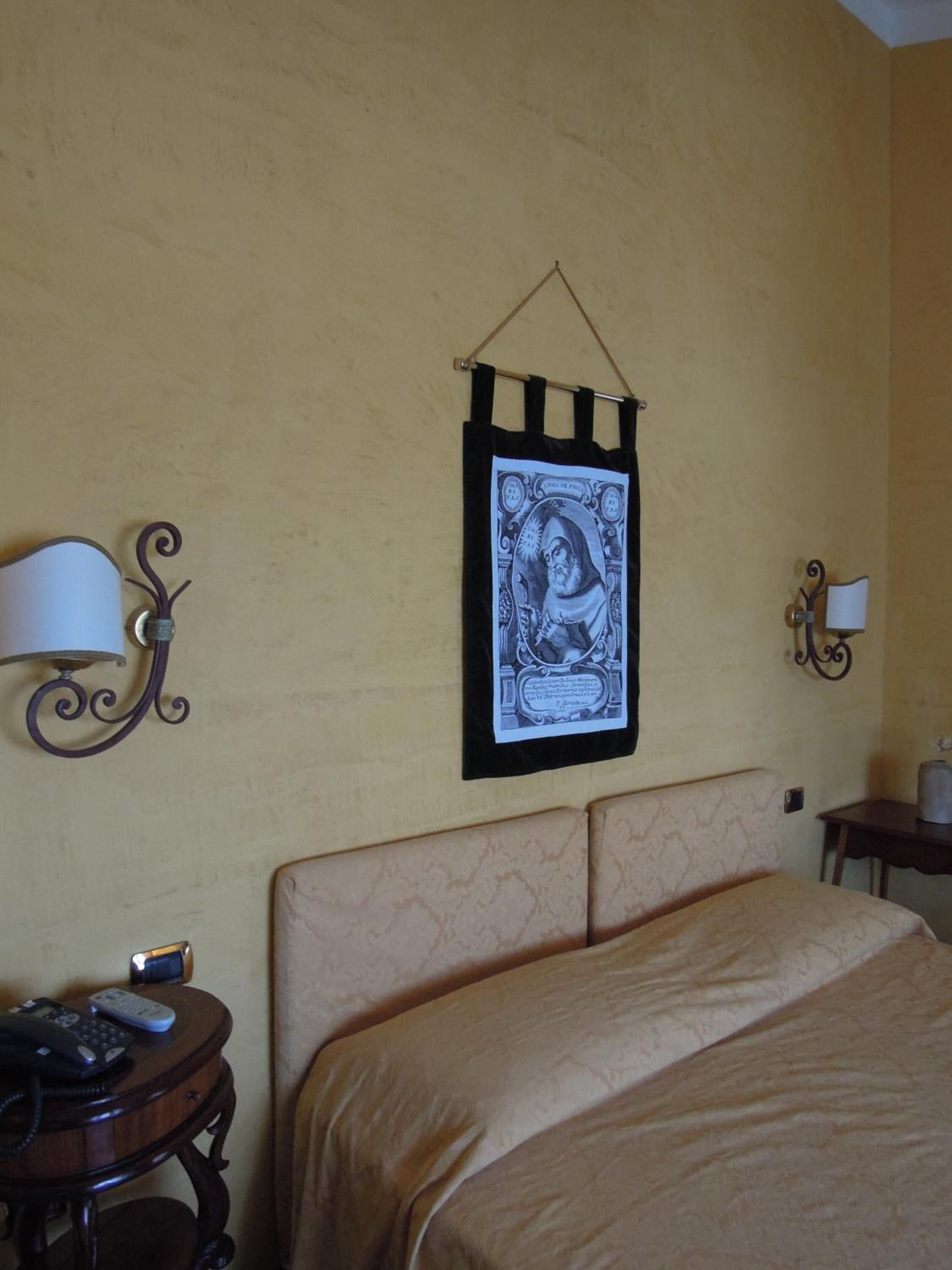 Una camera d'albergo con un letto, un comodino con una lampada e un'opera d'arte appesa al muro.