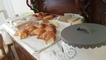 Un bufé de desayuno con cruasanes, pan y un recipiente con comida.