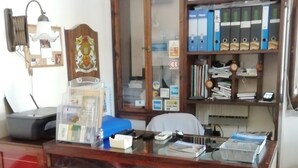 Un escritorio de madera con superficie de vidrio, una silla roja, un archivador con carpetas y un cuadro enmarco.