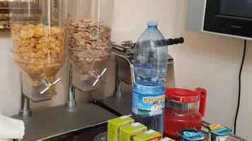 Una barra de desayuno con dispensadores de cereales, una botella de agua y diversas opciones de comida, incluyendo jugo de naranja y yogur.