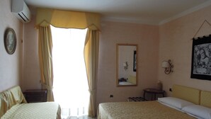 Habitación de hotel con dos camas, un espejo, una mesita pequeña y un aire acondicionado instalado en la pared.