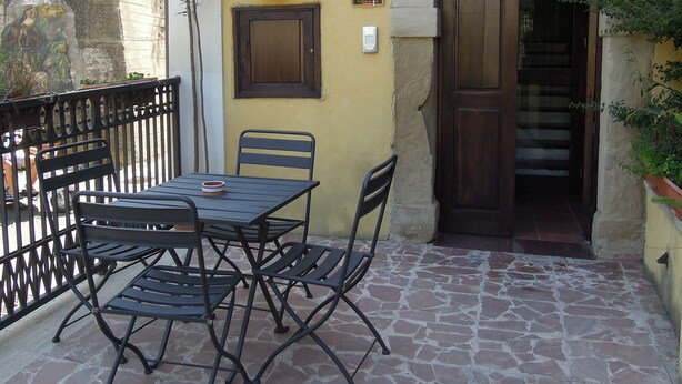 Un patio con una mesa y sillas, piso de piedra, pared amarilla, puerta de madera y un letrero que dice 'HOTEL SA'.