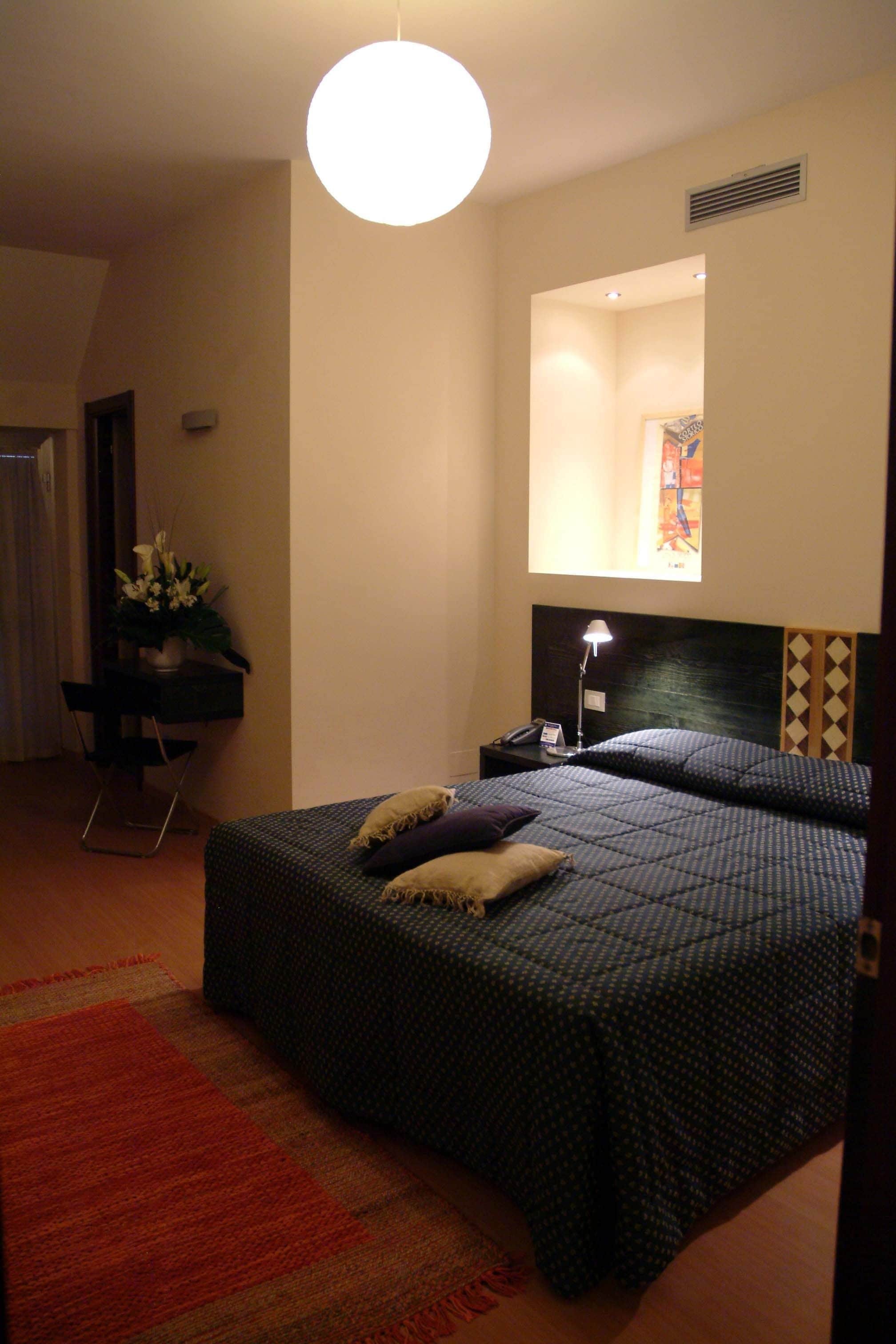 A bedroom with a bed, a desk, a chair, a lamp, and a mirror.