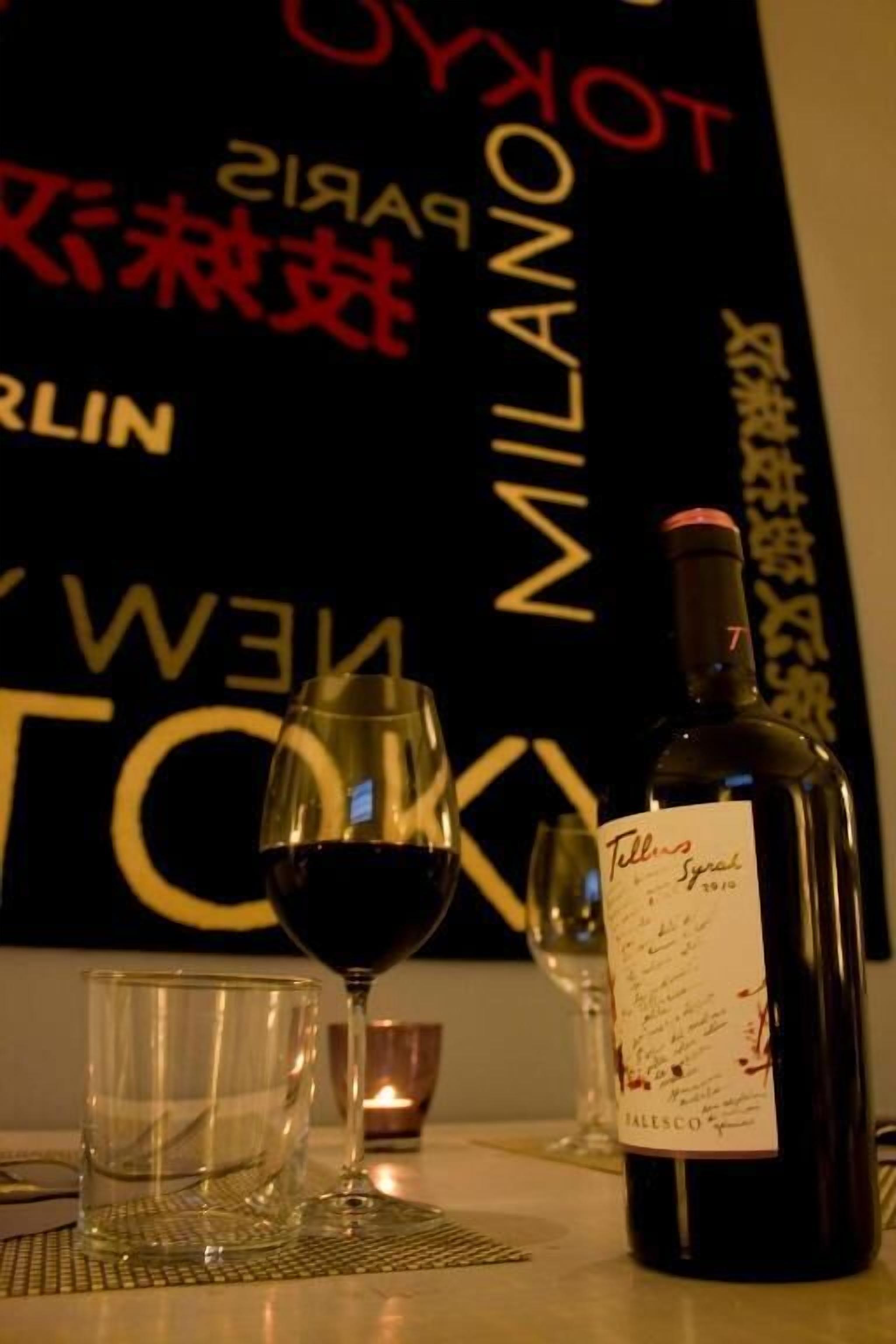 A bottle of wine and two glasses on a table with a placemat, set against a backdrop with various city names.
