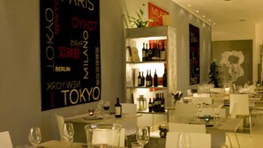 A restaurant with tables set for dining, a wall with city names, and a bar area with bottles. - Hotel Orvieto (Orvieto)