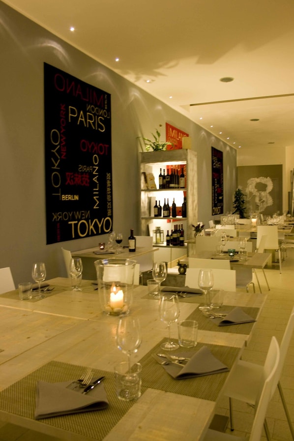 Un restaurante con mesas dispuestas para comer, una pared con nombres de ciudades y una zona de bar con botellas.