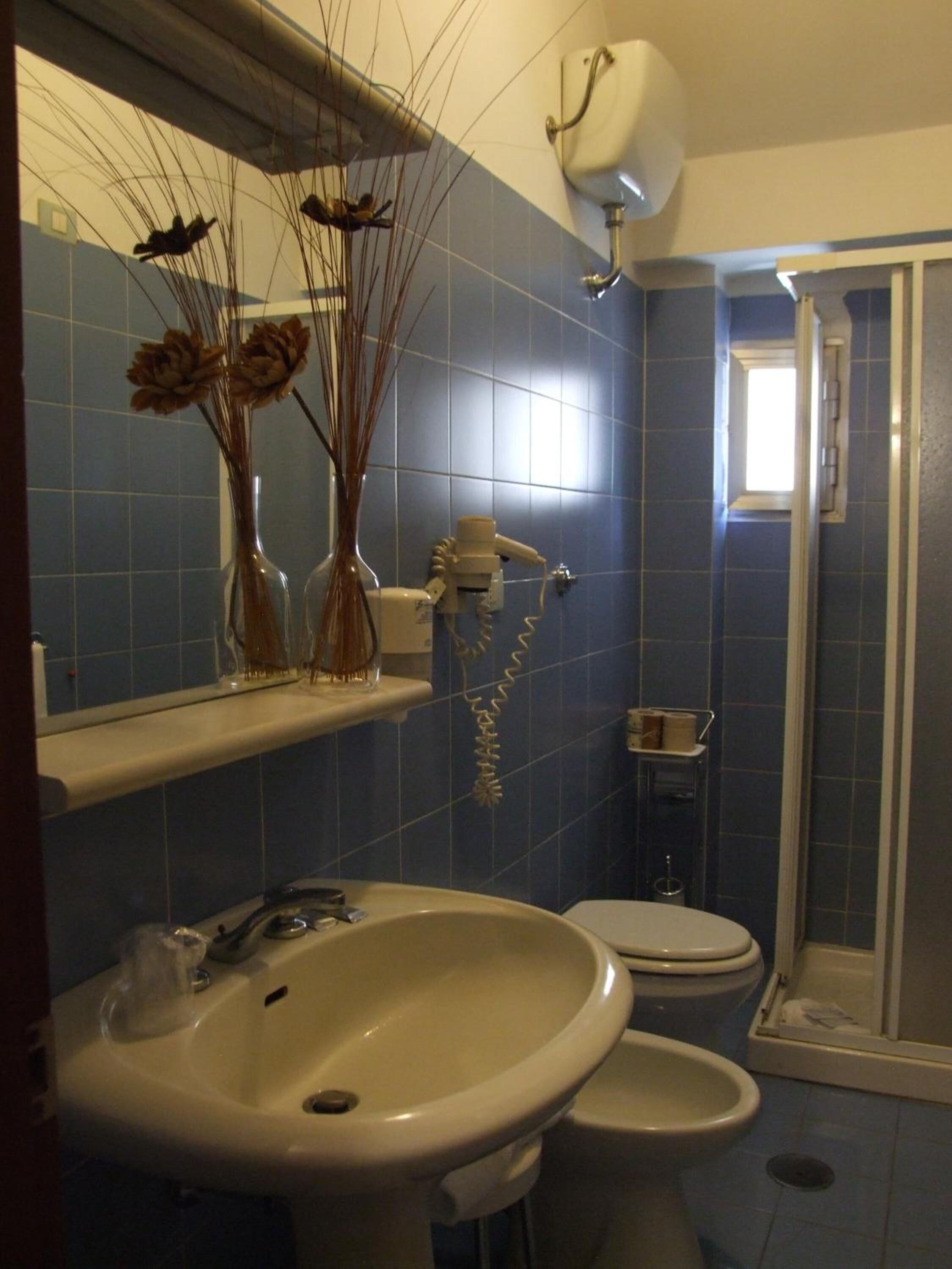 Een badkamer met een grote wastafel, toilet en douchegedeelte. Op de wastafel staan decoratieve vazen en boven het toilet een handdoekhouder.