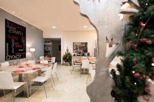A modern dining area with a long table set for a meal, a Christmas tree in the background, and a wall with city names in different languages.