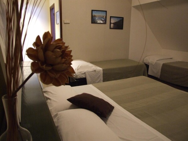 A hotel room with two beds, a vase with dried plants, and two framed pictures on the wall.