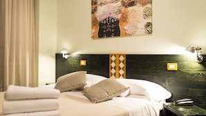 A hotel room with a bed, pillows, a headboard with a diamond pattern, wall-mounted lamps, and a painting. - Hotel Orvieto (Orvieto)