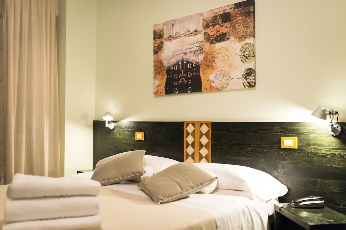 A hotel room with a bed, pillows, a headboard with a diamond pattern, wall-mounted lamps, and a painting.