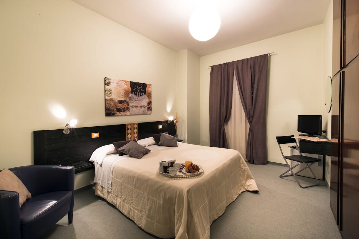 A hotel room with a bed, a desk, a chair, a television, and a wall-mounted artwork.