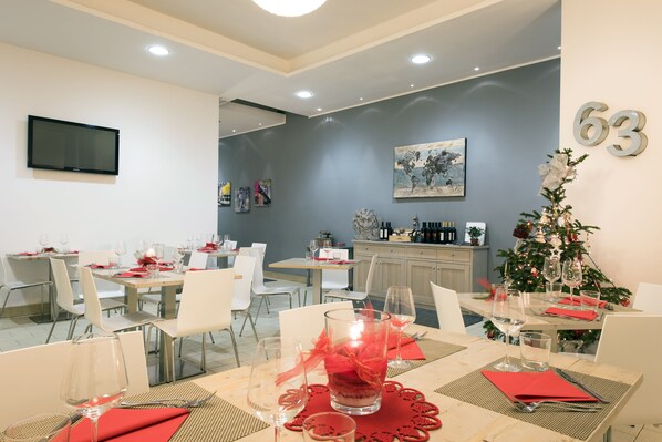 A dining area with multiple tables set for a meal, a television mounted on the wall, and a Christmas tree in the background. - Hotel Orvieto (Orvieto)