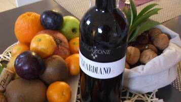 Een fles wijn met de naam 'Palazzo' op een tafel, samen met een fruitmand, noten en wijnkurken.