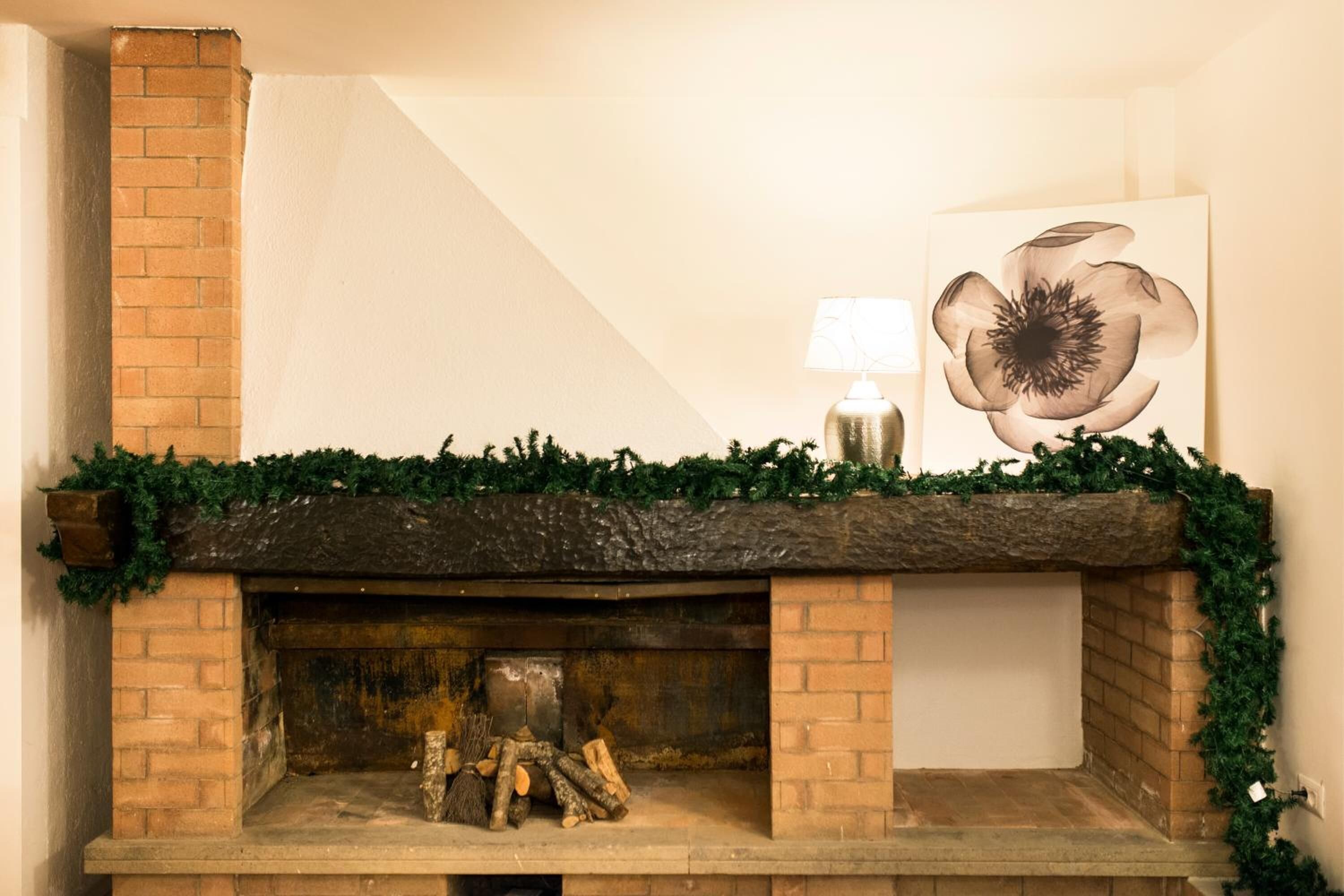 Une cheminée avec un manteau en briques, décorée de verdure et d’une lampe.