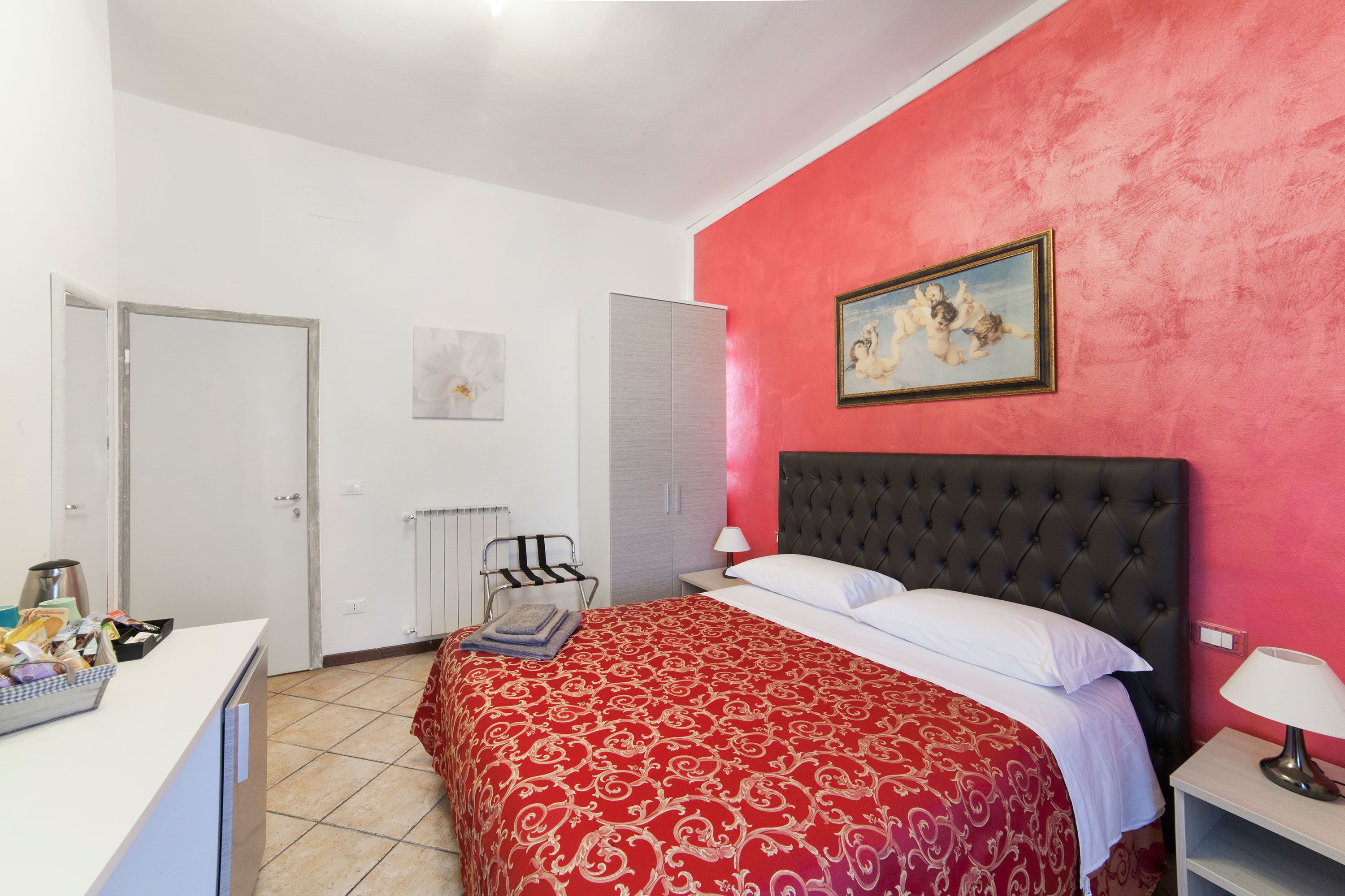 A bedroom with a red wall, a large bed with white bedding, a black headboard, and a painting above the bed.